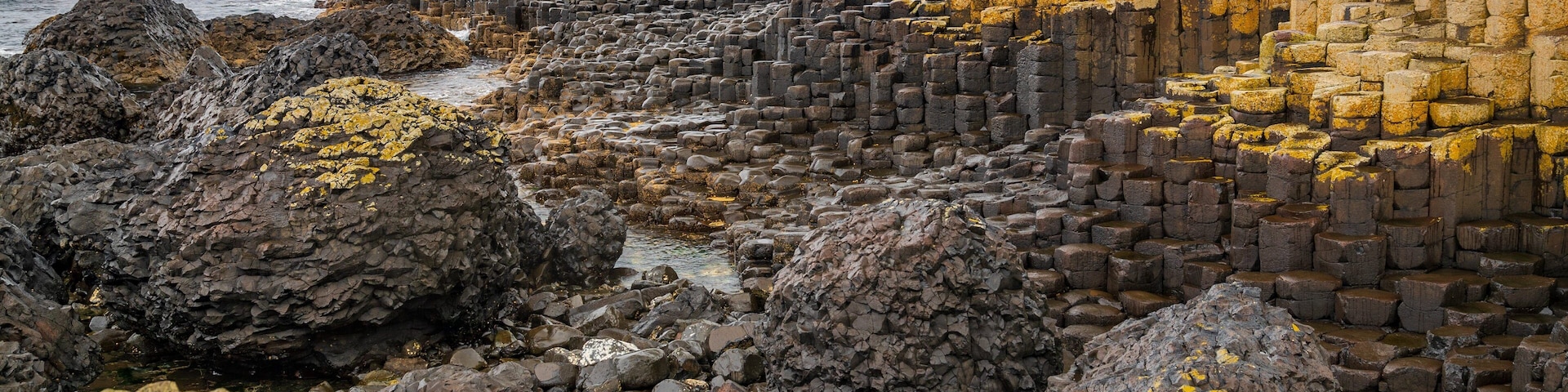Paisagem costeira rochosa com formações de pedra em camadas e rochas cobertas de líquenes.