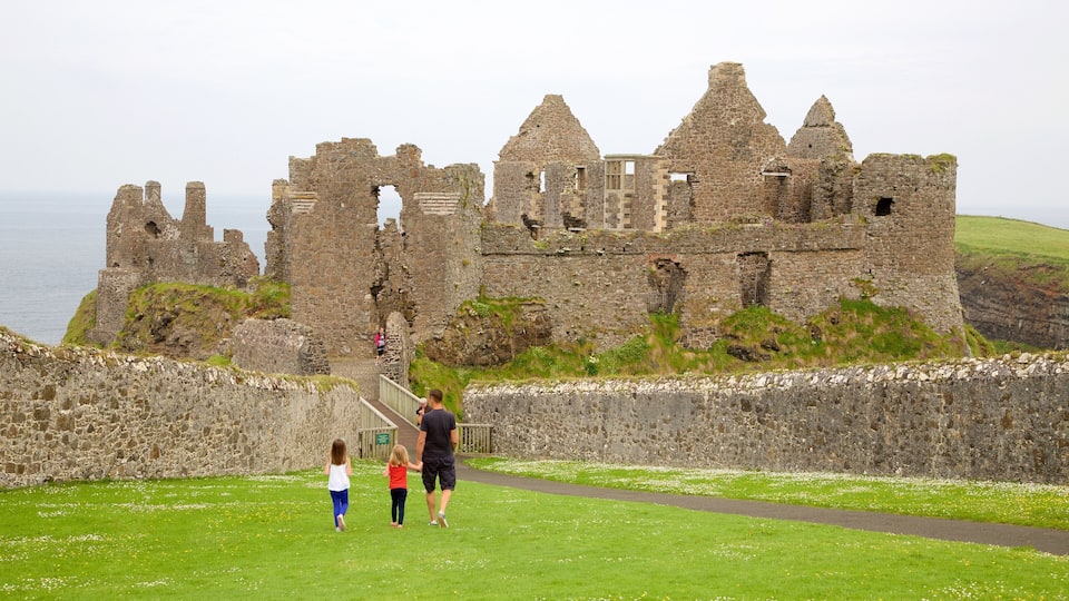 A historic stone castle with ruins, a grassy pathway, and a body of water in the background.