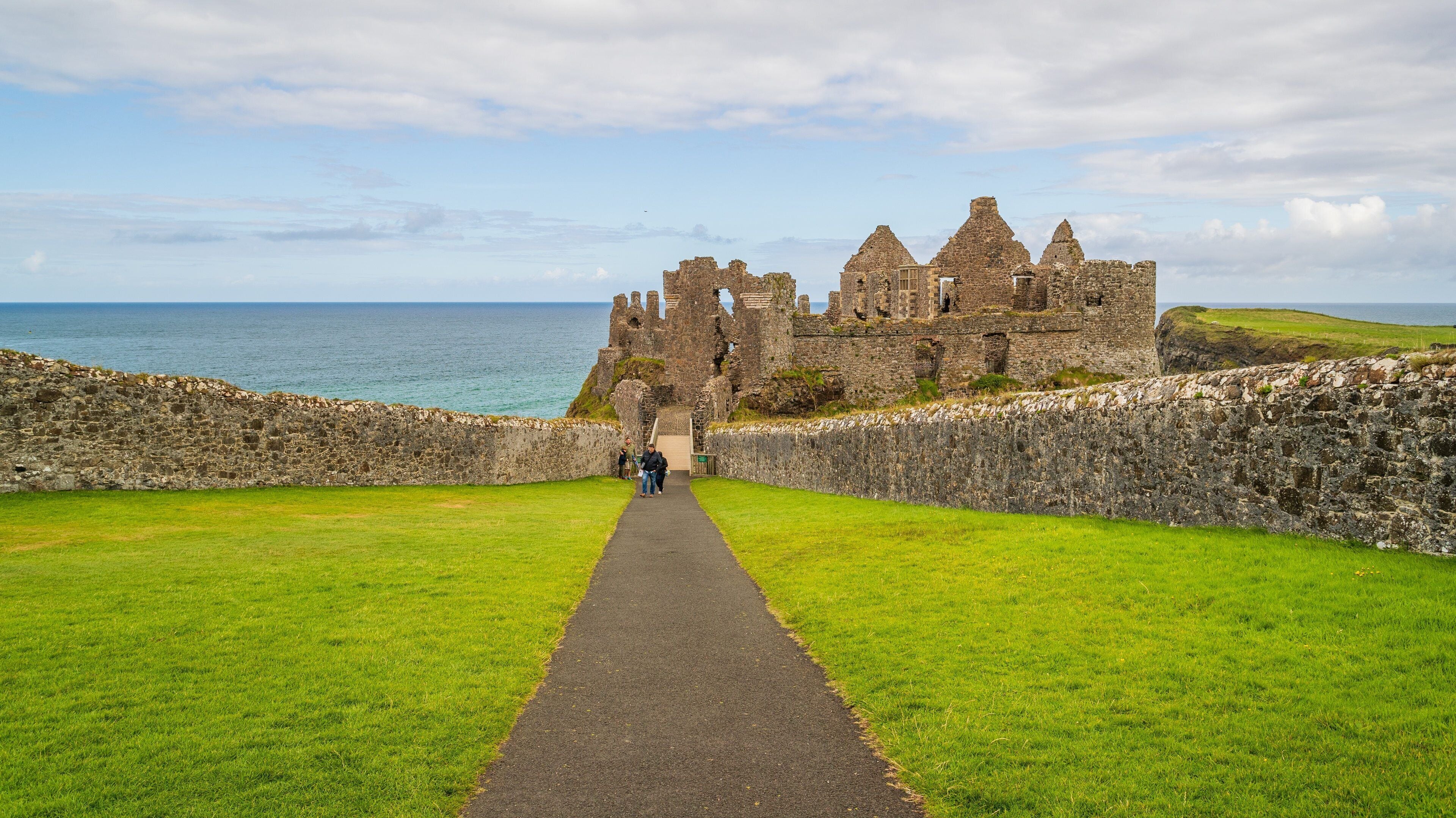 A castle with a grassy pathway leading to it, overlooking the sea.
