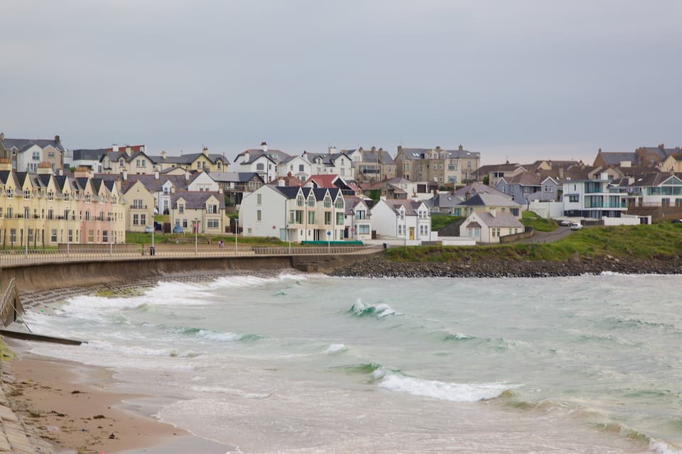 A coastal town with houses along the beach and waves crashing onto the shore.