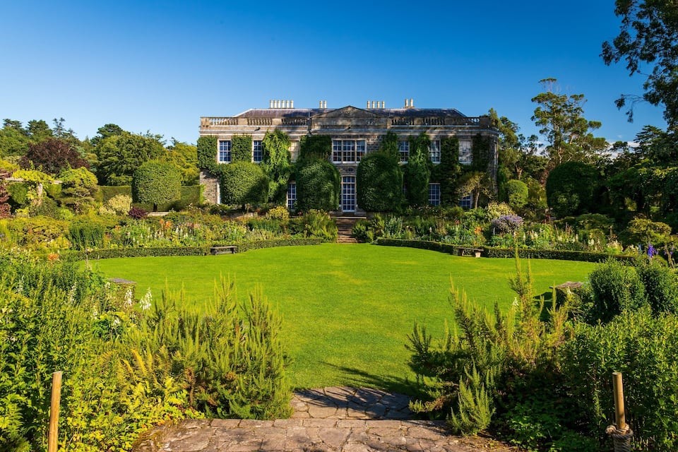 A large, historic building surrounded by lush gardens and a well-maintained lawn.