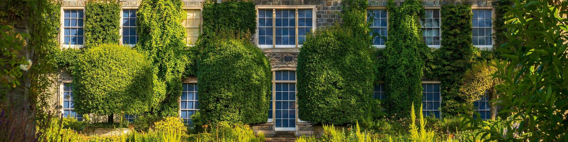 A large, historic building with a symmetrical facade, surrounded by lush greenery and a well-maintained lawn.