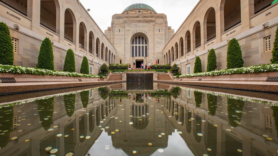 A symmetrical building with arched windows and a central dome, surrounded by a reflective water feature with floating objects.