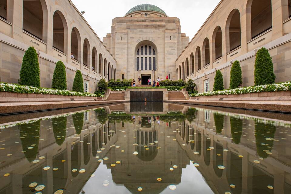 A symmetrical building with arched windows and a central dome, surrounded by a reflective water feature with floating objects.