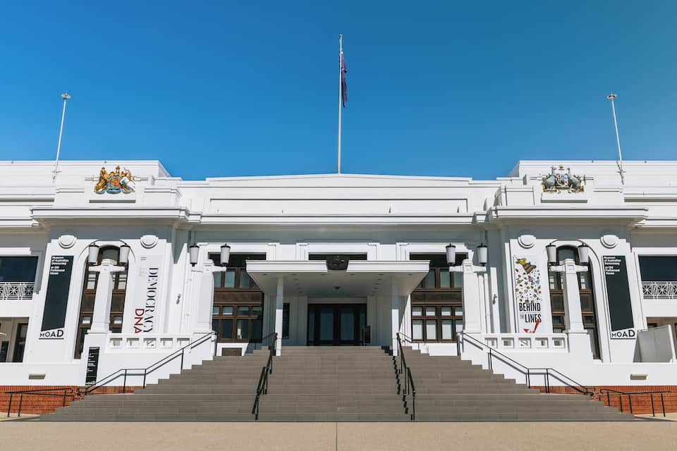 A white building with a flagpole, steps, and a coat of arms.