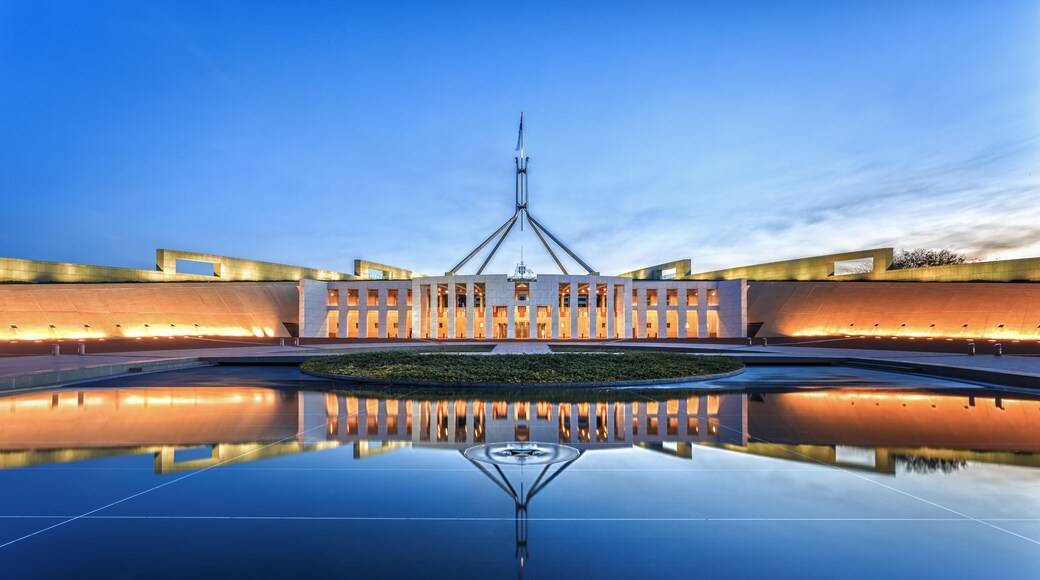 A modern building with a central spire, surrounded by a reflective water surface.