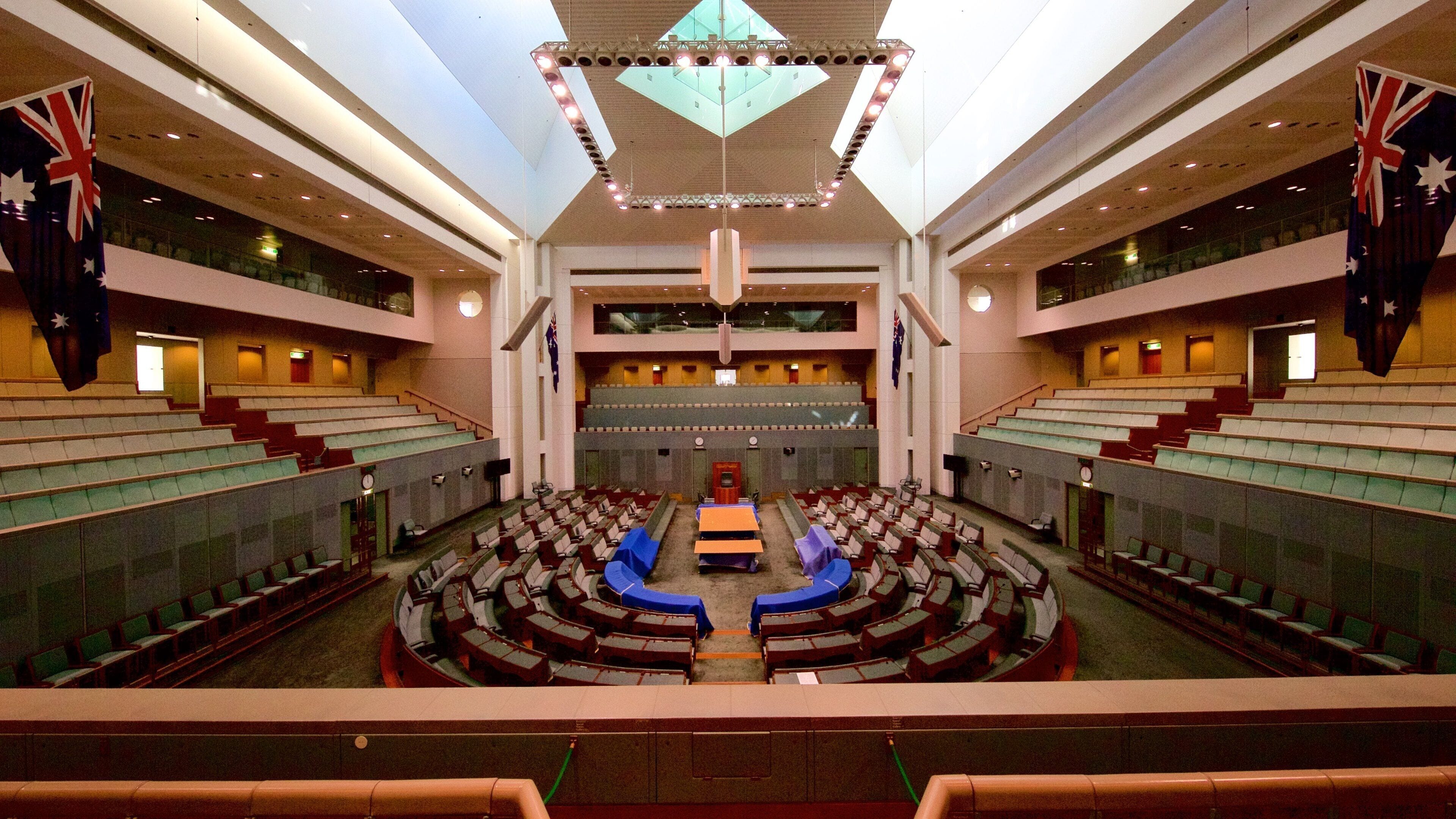 Un gran auditorio moderno con asientos escalonados, un escenario central y banderas australianas.