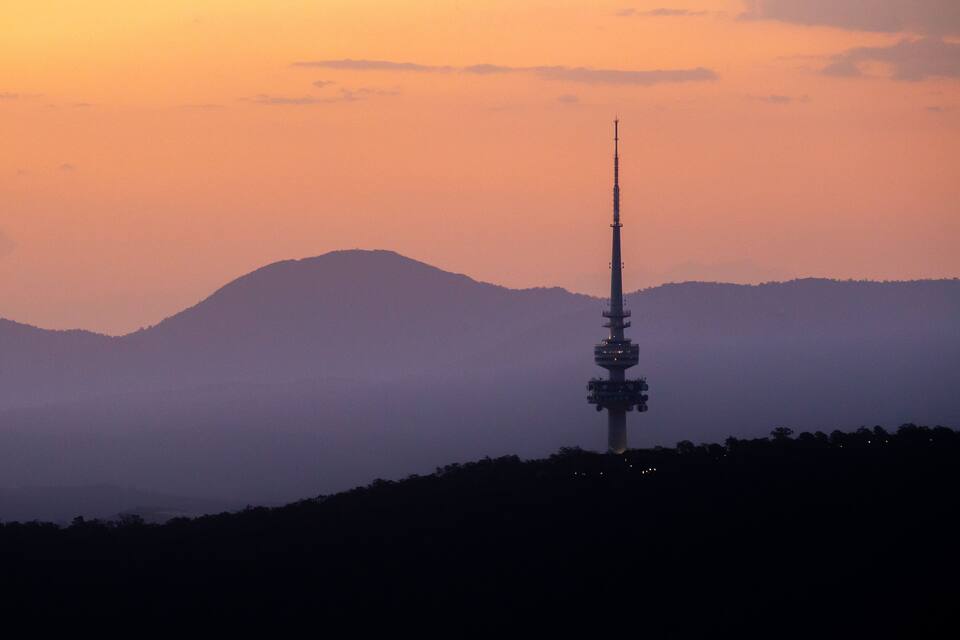 A tower silhouetted against a sunset sky, surrounded by hills.