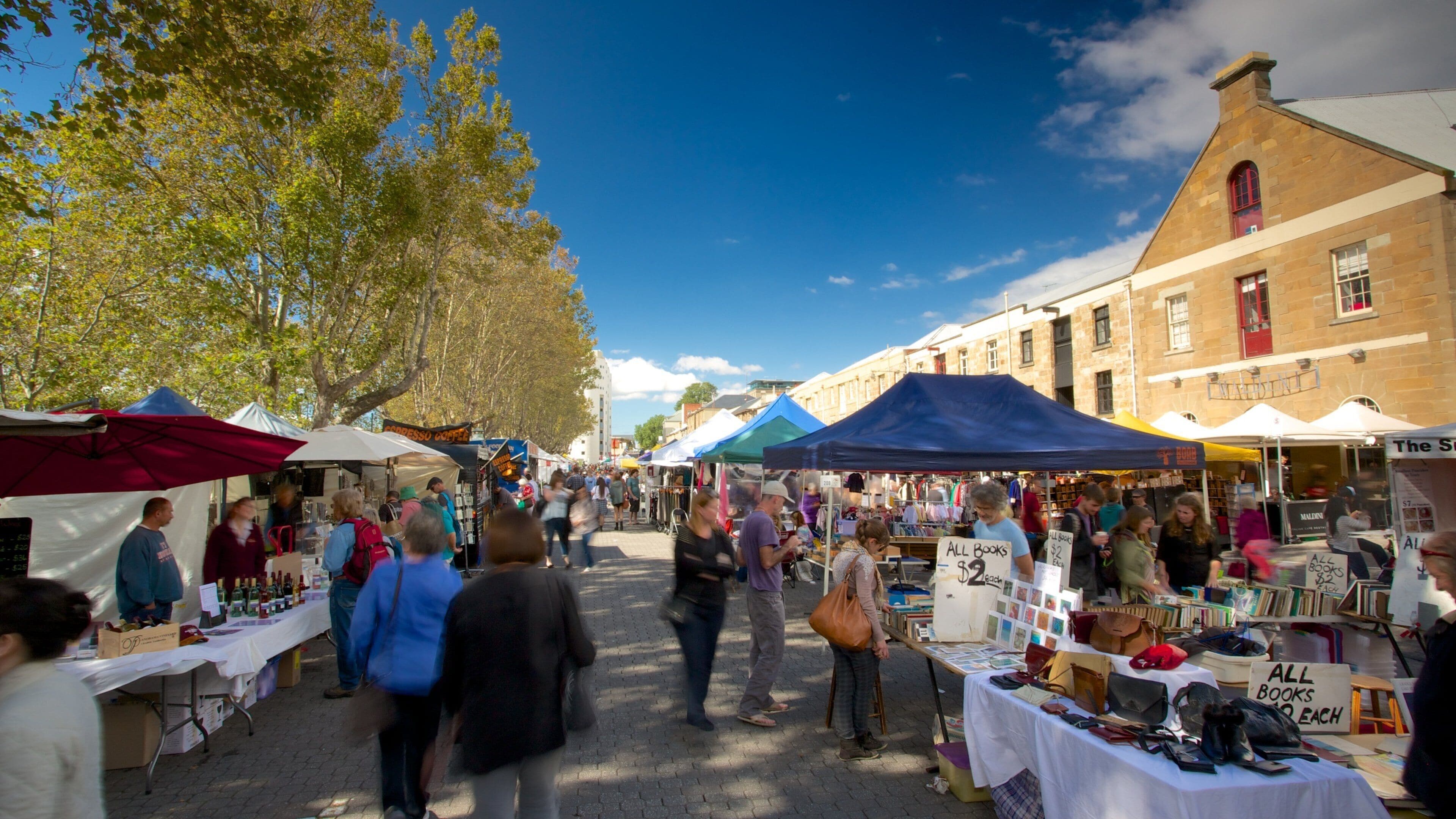 A busy outdoor market with various stalls selling books and other items.