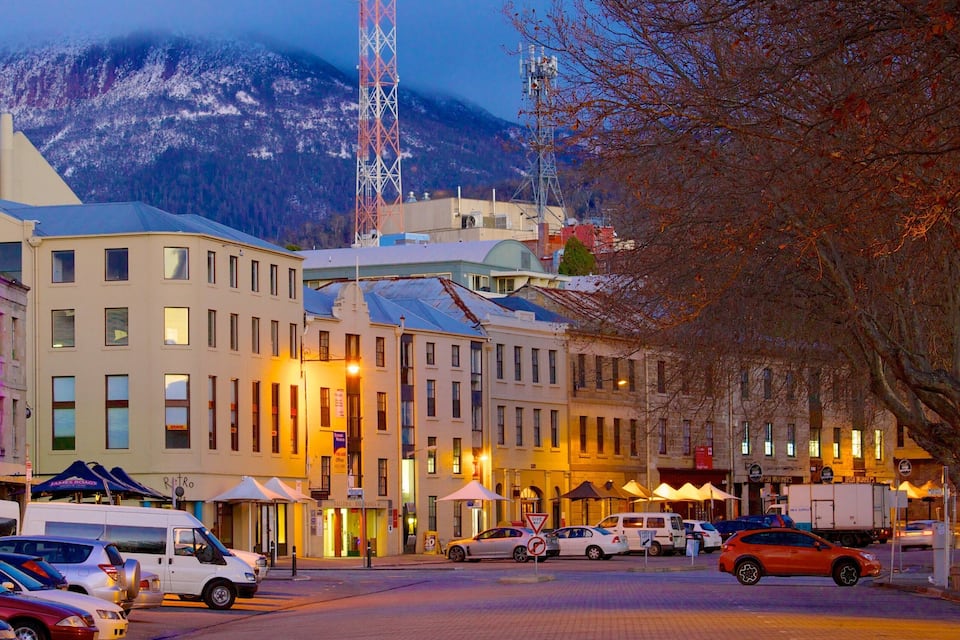 Una calle urbana con edificios, automóviles y una montaña al fondo.