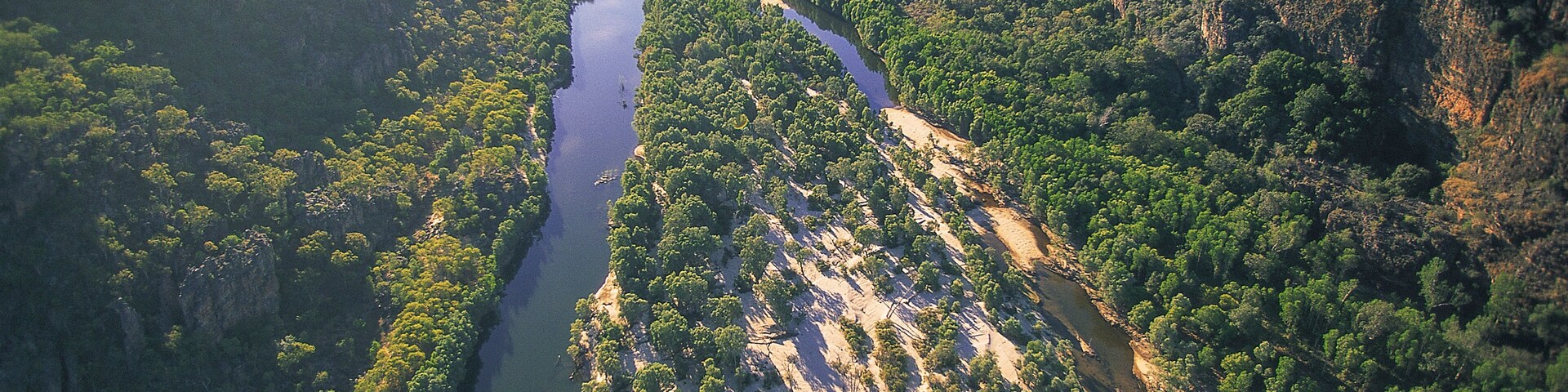 Um rio serpenteando por um cânion com vegetação densa e penhascos íngremes.