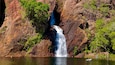 Ein Wasserfall stürzt über eine felsige Klippe, umgeben von üppiger Vegetation.
