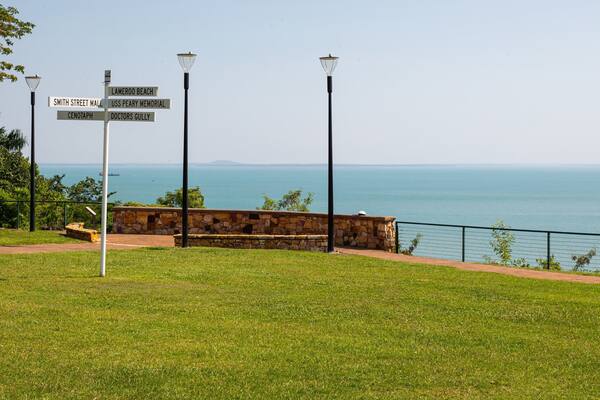 Uma área gramada com um muro de pedra e um sinalizador indicando direções para Smith Street Mall, Lameroo Beach, USS Peary Memorial, Doctors Gully e Cenotaph.
