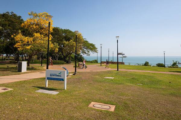 En park med et skilt for Darwin Bicentennial Park, en sti og udsigt over havet.