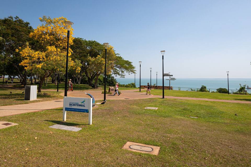 Un parque con un cartel que indica el Parque Bicentenario de la Ciudad de Darwin, un sendero para caminar y vista al océano.
