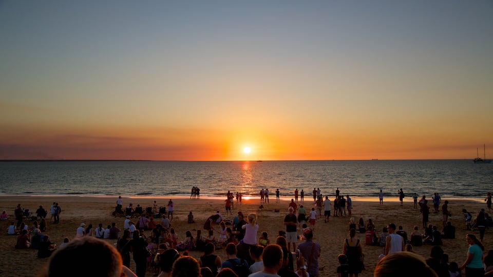 Um pôr do sol sobre uma praia cheia de gente apreciando a paisagem.