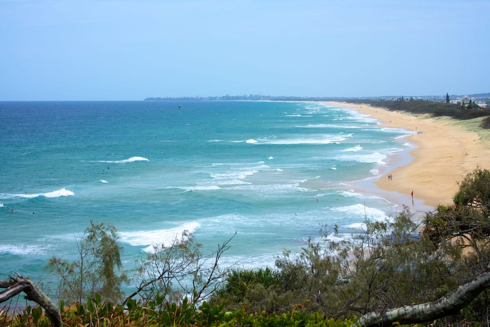 A coastal beach with waves, a sandy shore, and a distant city skyline.