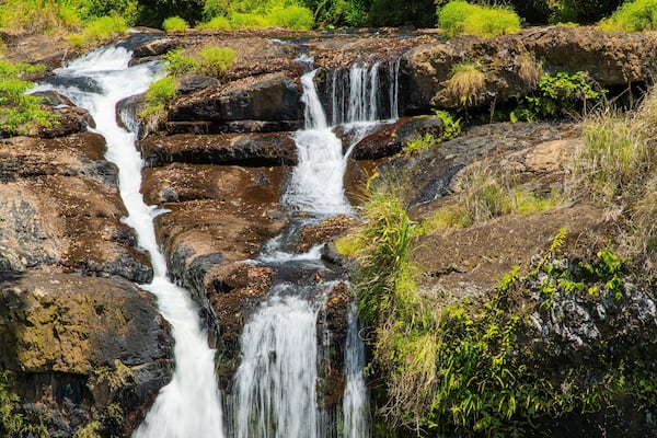 A multi-tiered waterfall cascading over rocky terrain surrounded by lush greenery.