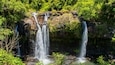 A waterfall cascading over a rocky cliff surrounded by lush greenery.