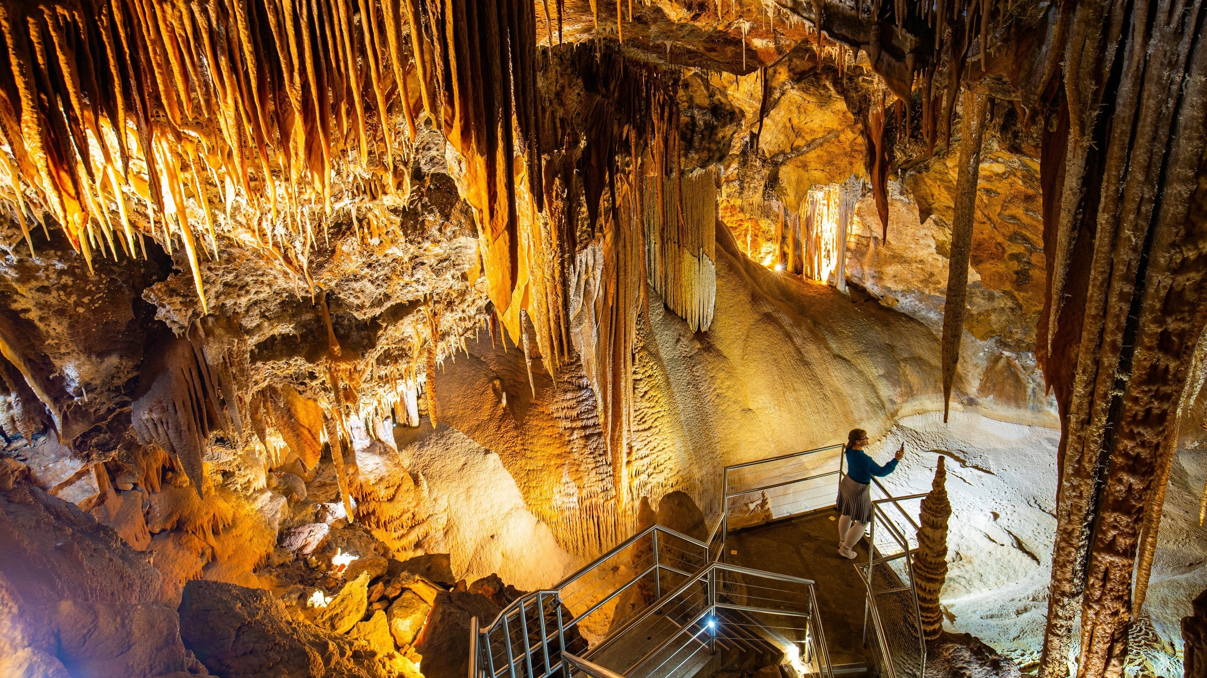 Eine Höhle mit Stalaktiten und Stalagmiten, eine Person macht ein Foto, und es gibt Metallgeländer.