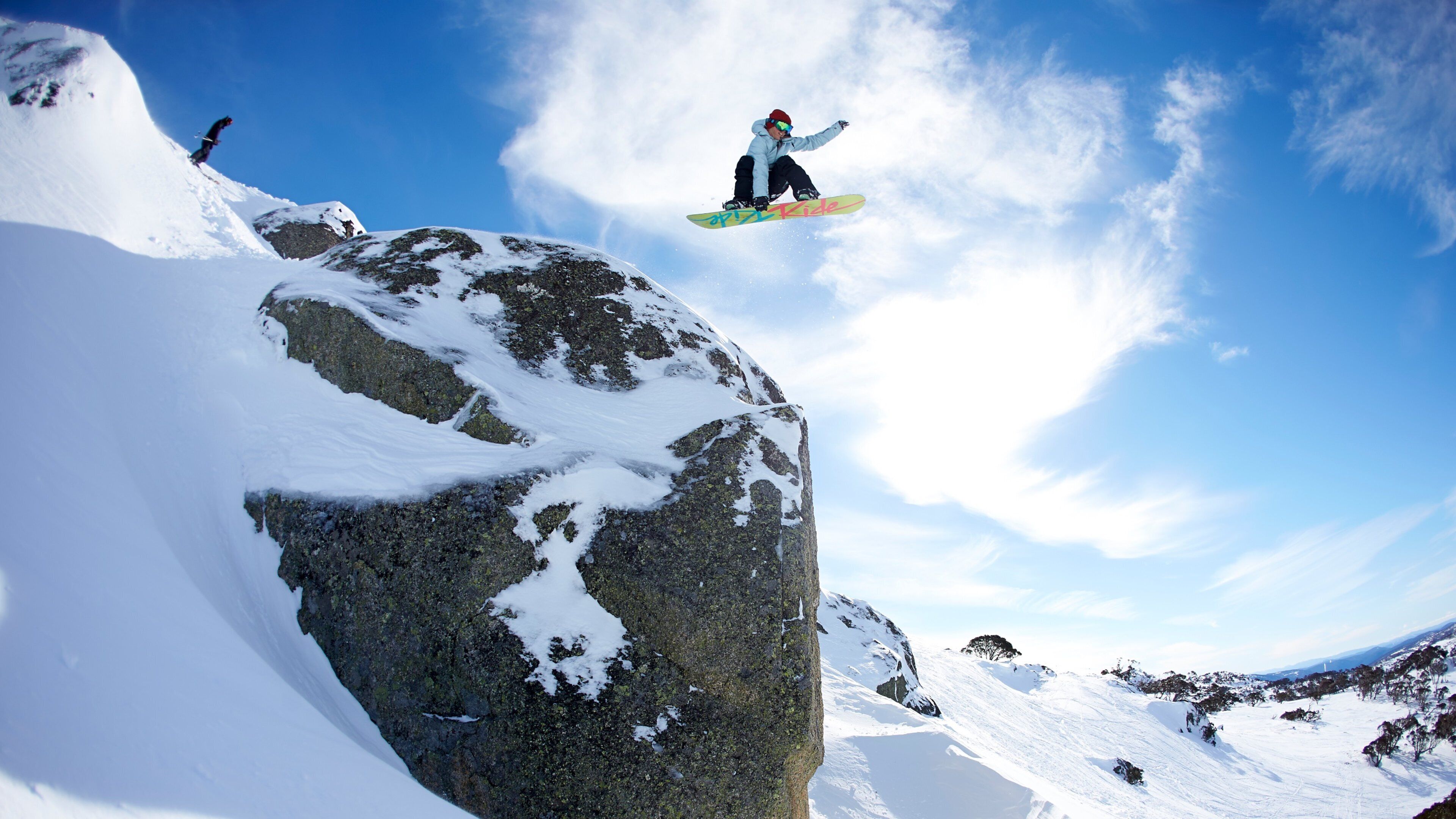 A snowboarder mid-air above a snow-covered rock.