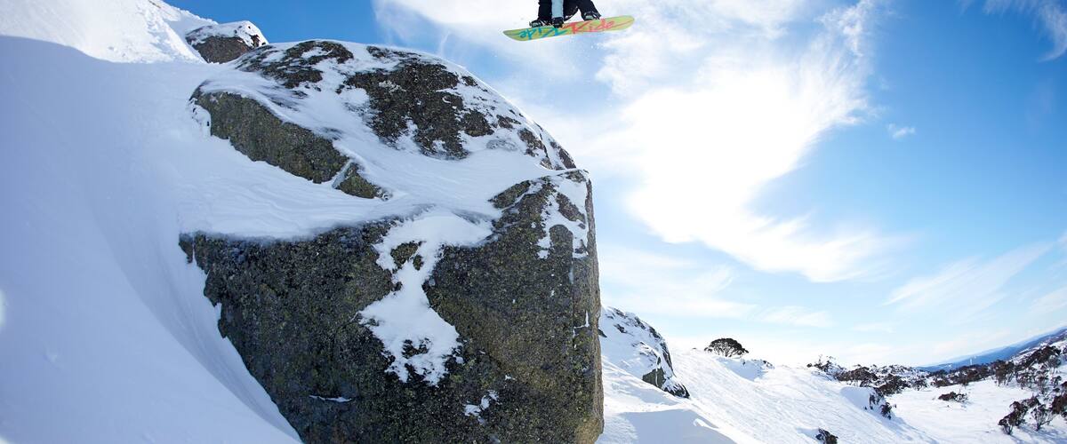 A snowboarder mid-air above a snow-covered rock.