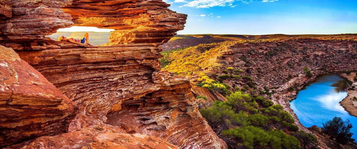 A canyon with layered red rock formations, a river, and a bridge in the distance.