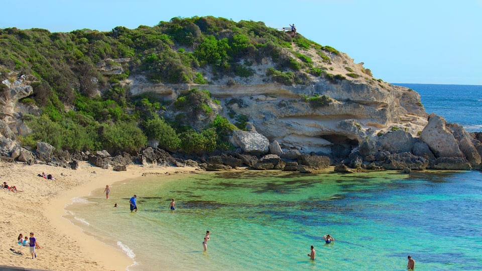 A beach with clear turquoise water, sandy shore, and rocky cliffs with greenery.