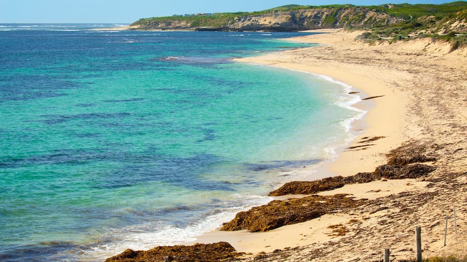 A sandy beach with clear turquoise waters and rocky outcrops.