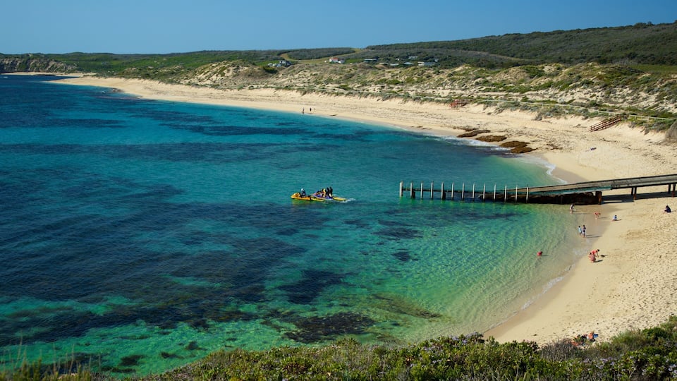 A beach with clear turquoise water, a sandy shore, and a pier extending into the sea.