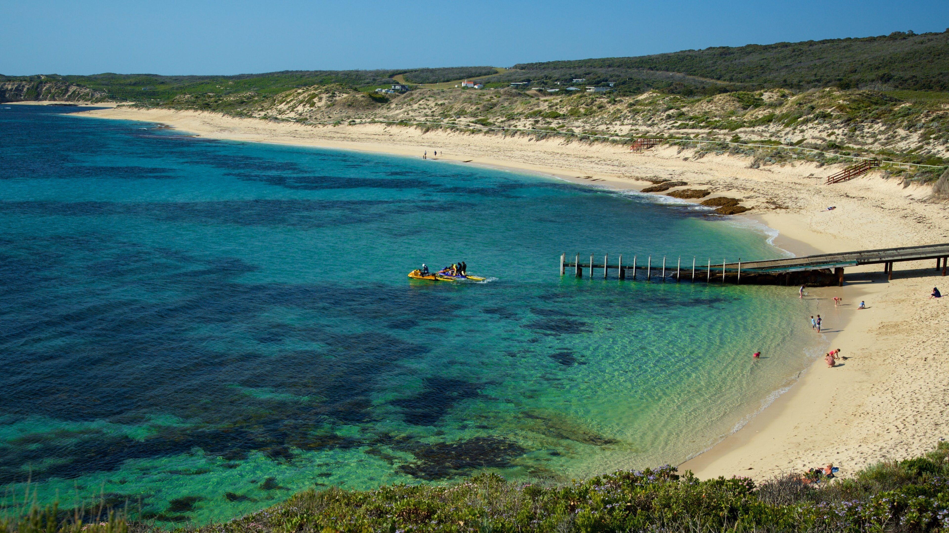 A beach with clear turquoise water, a sandy shore, and a pier extending into the sea.
