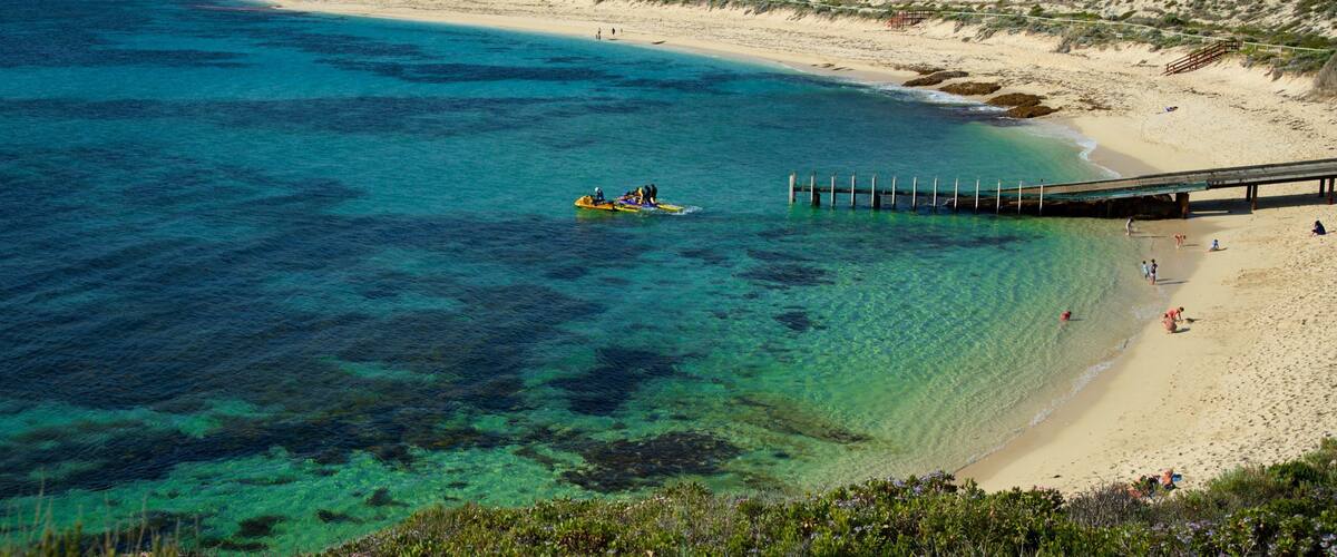 A beach with clear turquoise water, a sandy shore, and a pier extending into the sea.