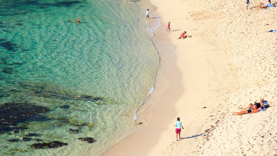 A beach with clear turquoise water, sandy shore, and people sunbathing and swimming.