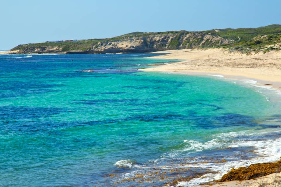 A beach with clear turquoise waters, sandy shore, and rocky cliffs.