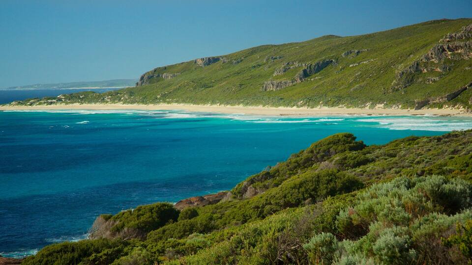 A coastal landscape with a beach, clear blue waters, and green hills.