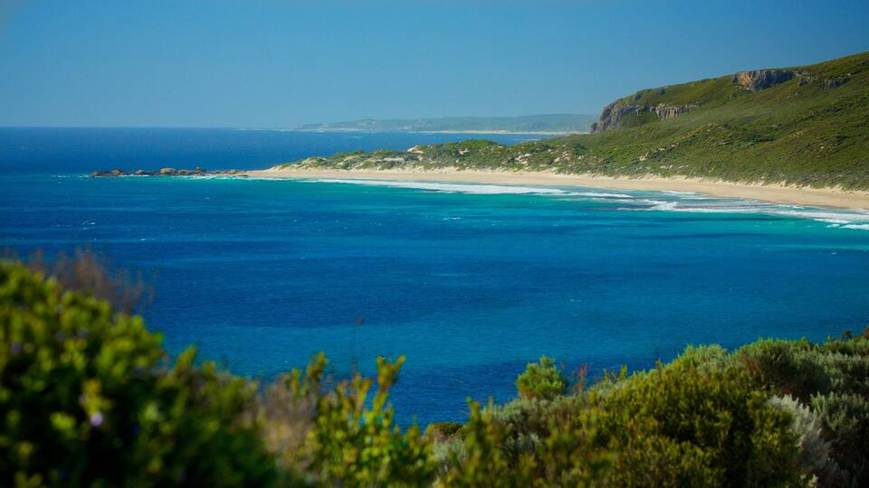 A coastal landscape with a clear blue sea, sandy beach, and green hills.
