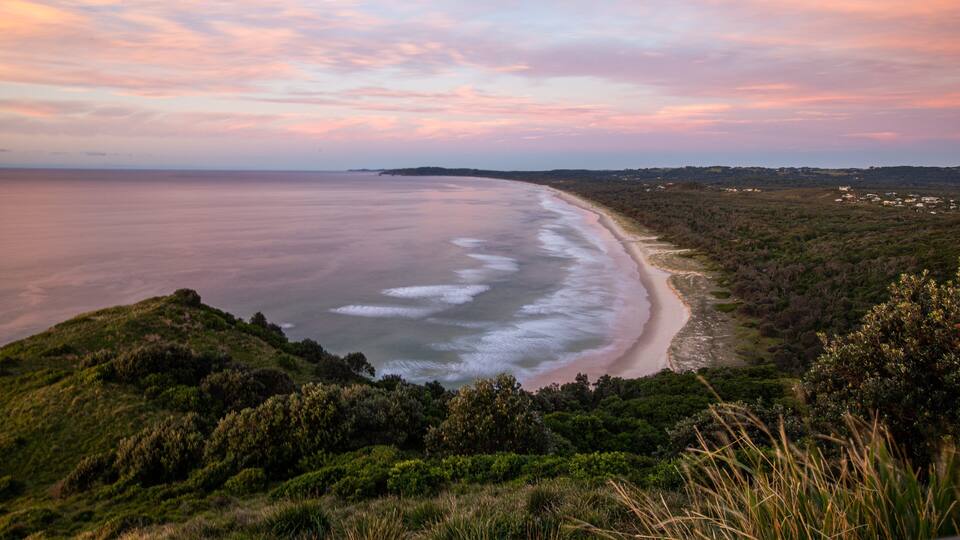 A coastal landscape with a beach, dense greenery, and a distant town.