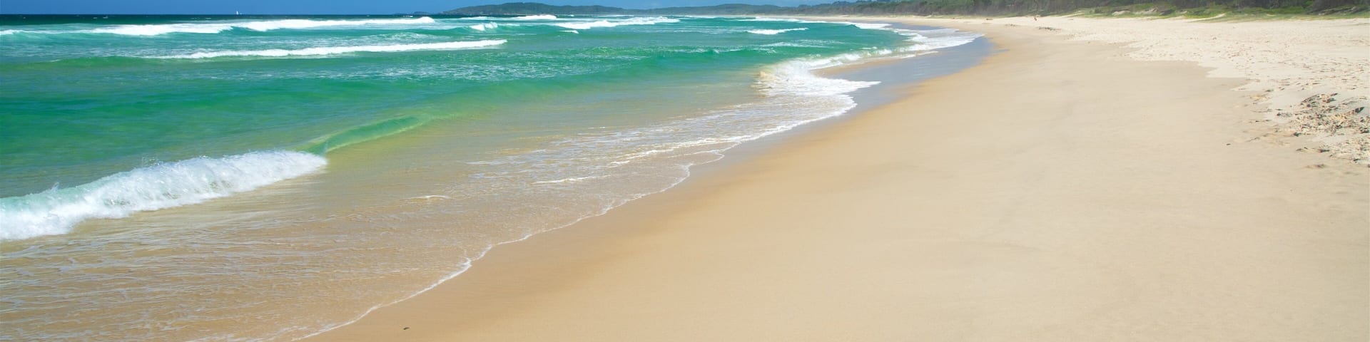 A wide sandy beach with gentle waves and a clear blue sky.