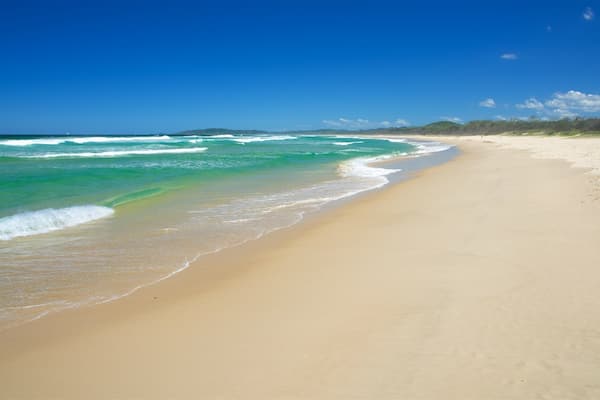 Une vaste plage de sable fin, avec des vagues douces et un ciel bleu dégagé.
