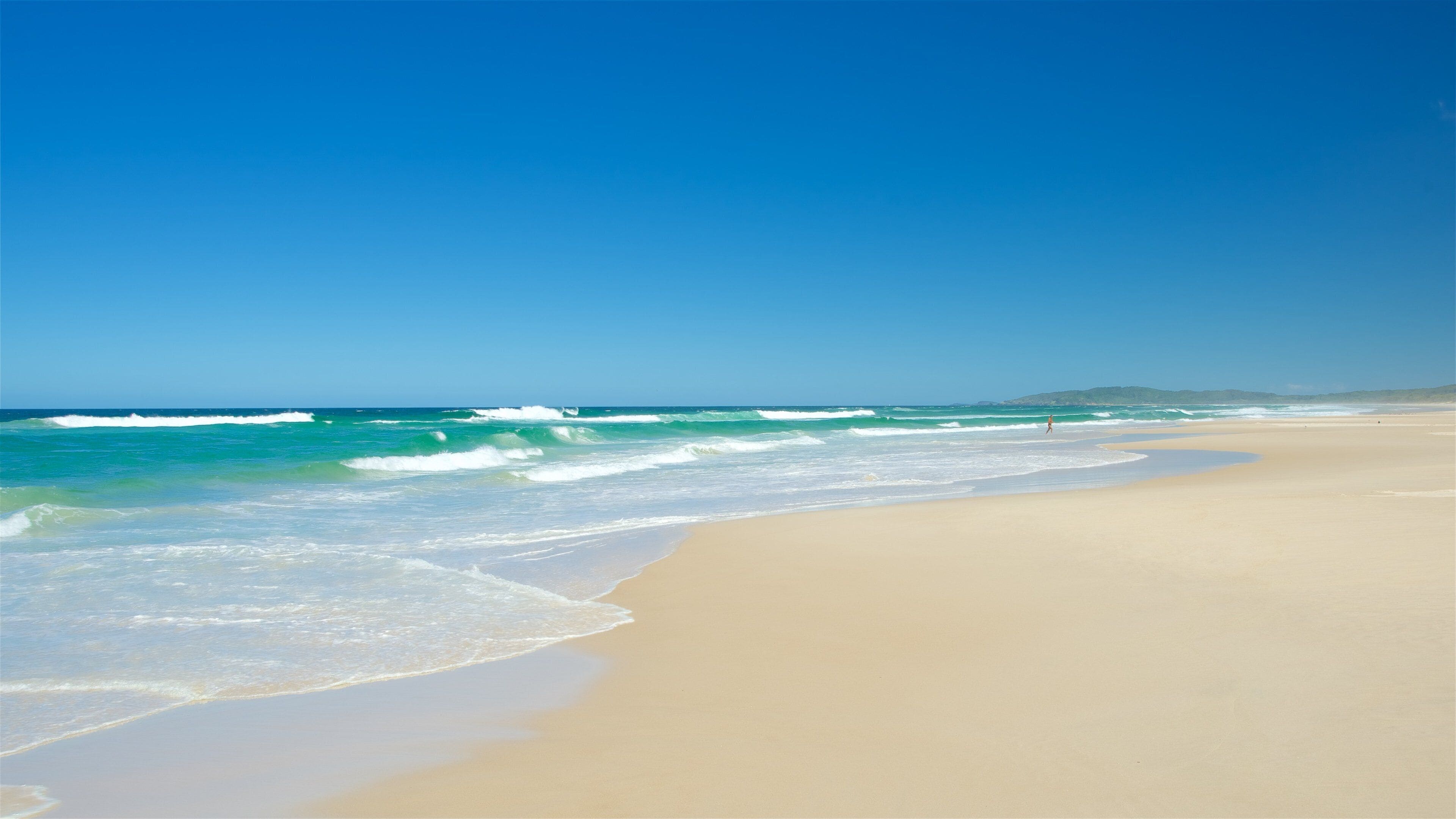 A sandy beach with waves crashing onto the shore and a clear blue sky.