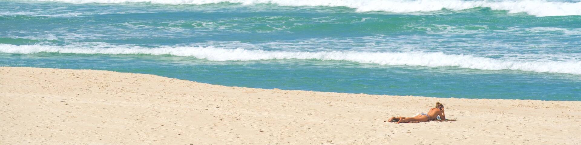 A beach with waves crashing against rocky cliffs and a clear blue sky.