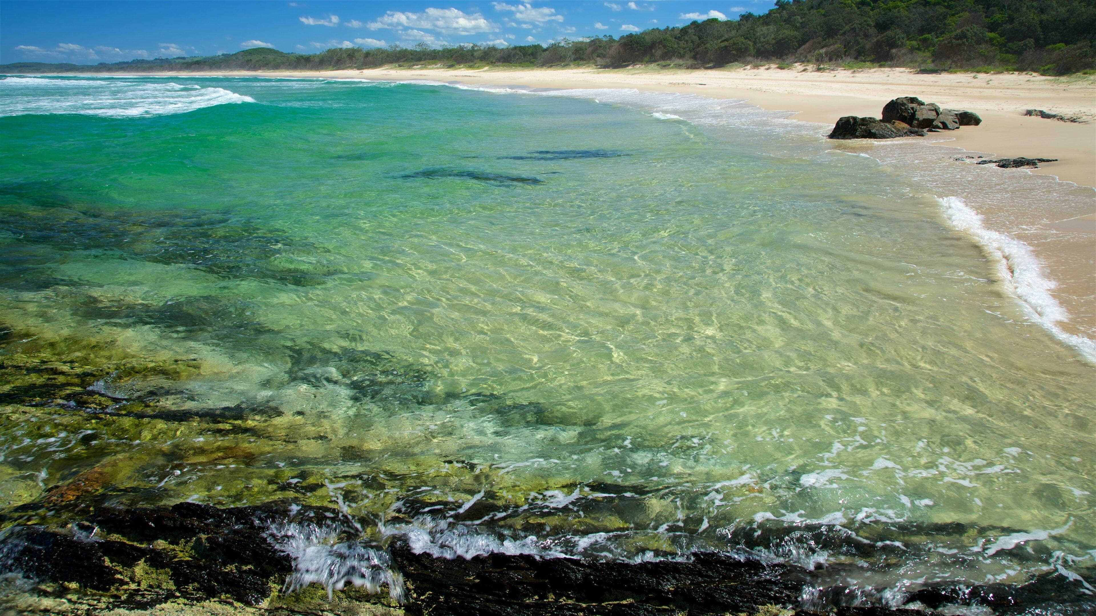 A clear coastal beach with turquoise water, sandy shore, and rocky outcrops.