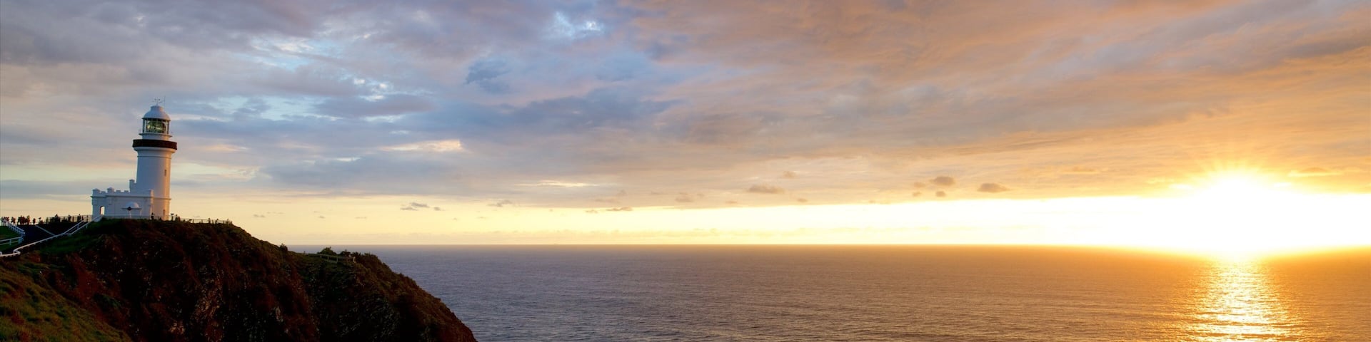 Faro de Cabo Byron que incluye una puesta de sol y costa escarpada
