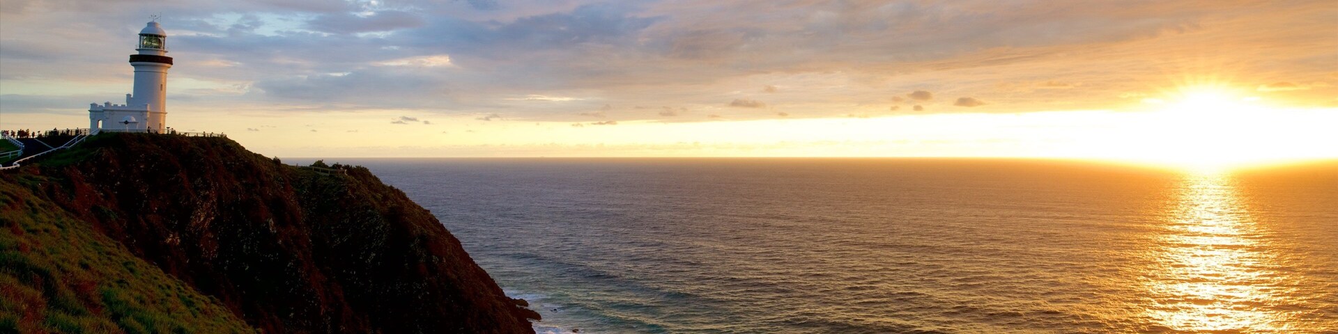 A lighthouse on a cliff overlooking the ocean at sunset.