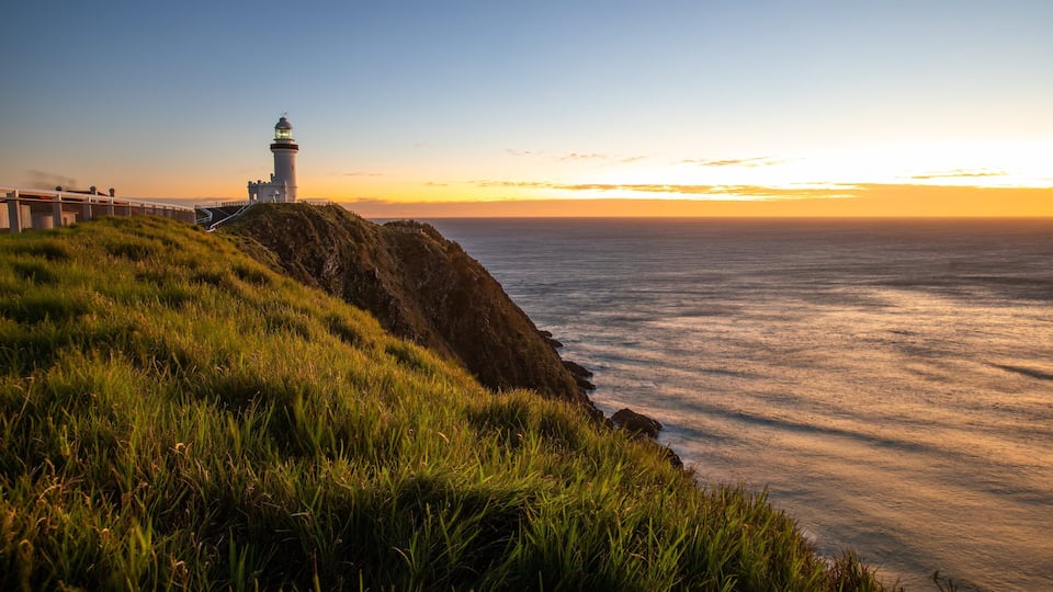 A lighthouse on a grassy cliff overlooking the ocean at sunset.