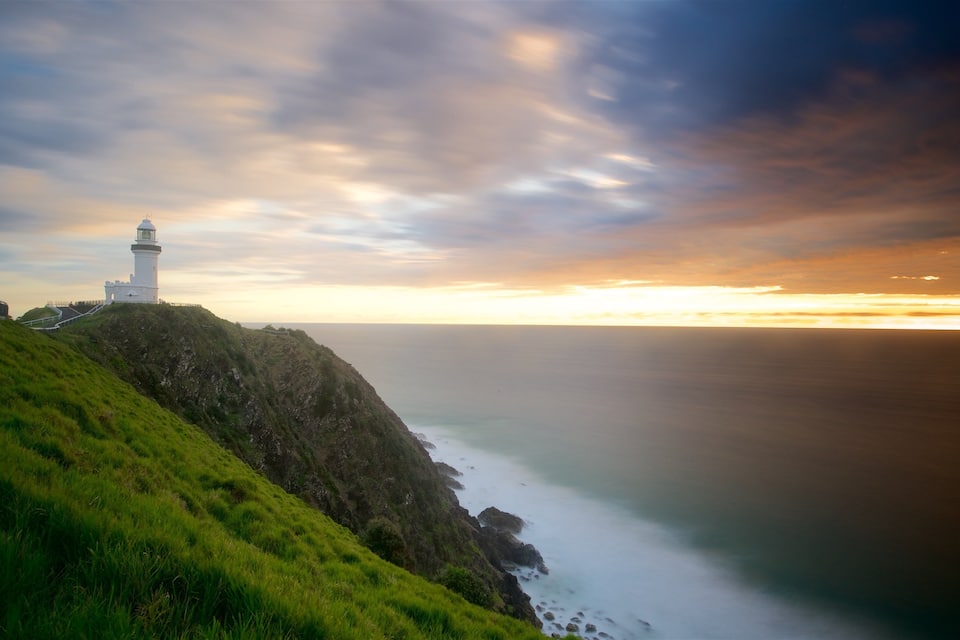 A lighthouse on a grassy cliff overlooking the ocean at sunset.