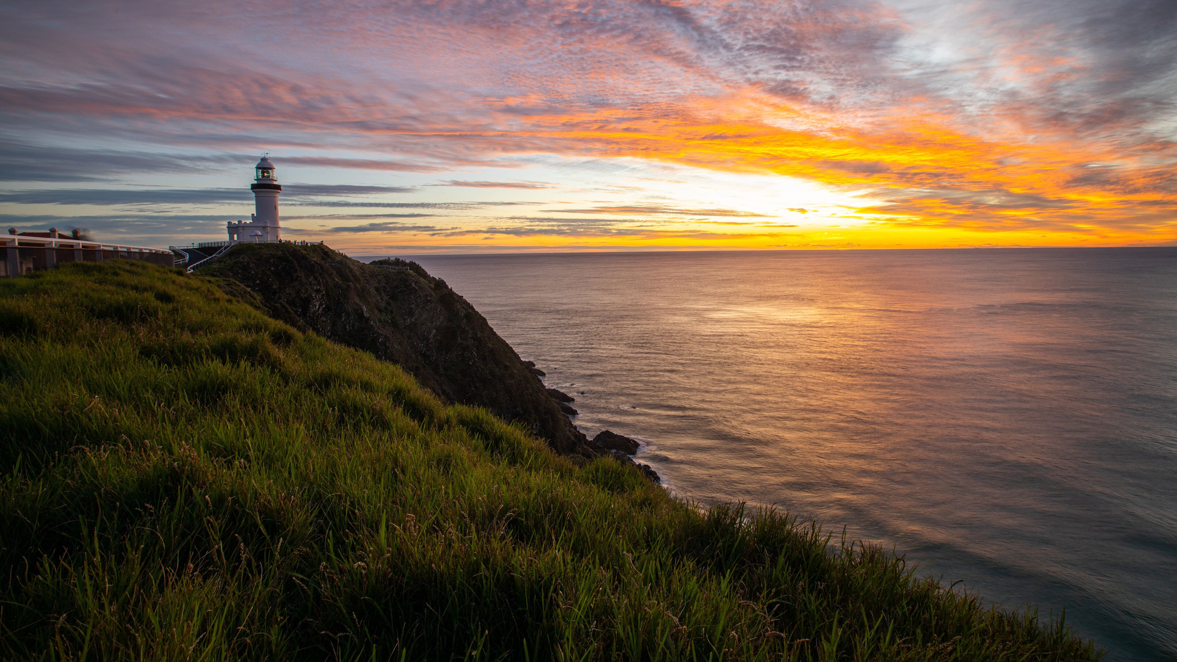 A lighthouse on a grassy cliff overlooking the ocean at sunset.