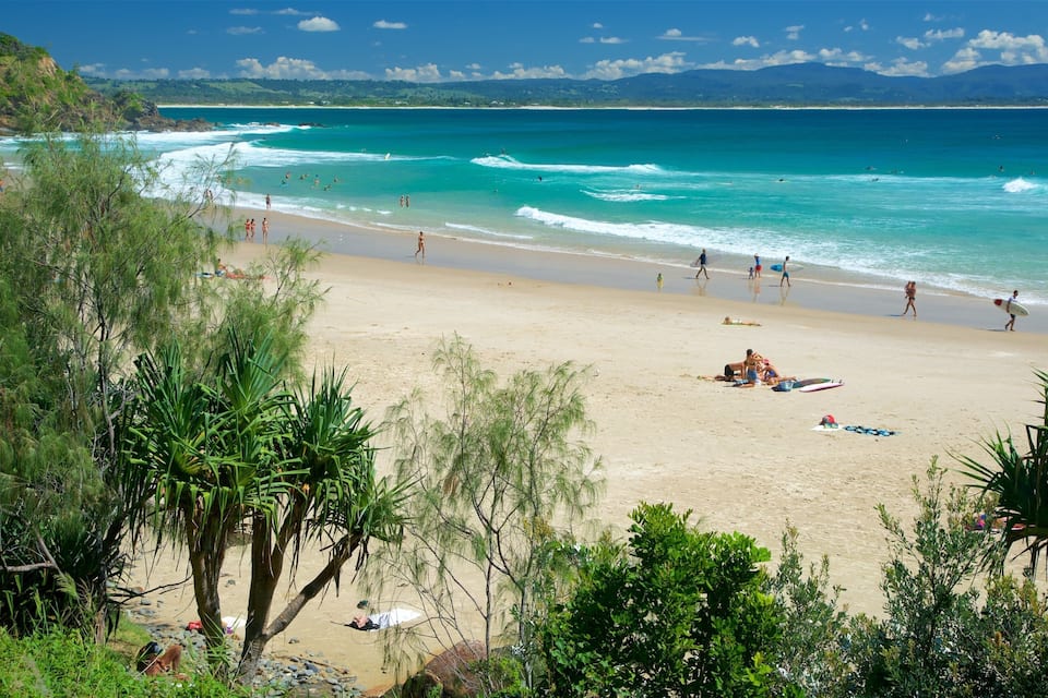 A beach with clear turquoise waters, people sunbathing, and surfers.