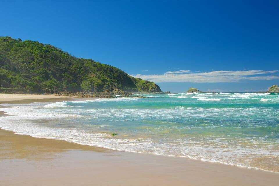 A beach with turquoise waters, a sandy shore, and a forested hill.