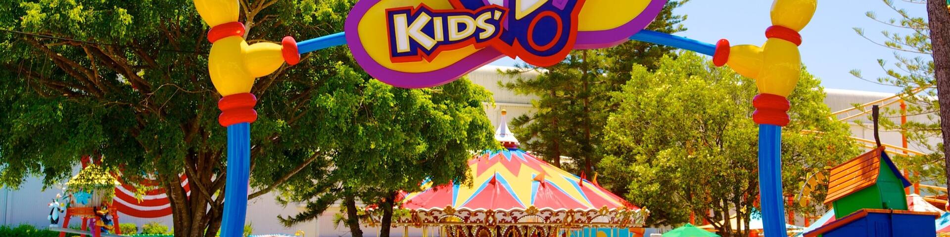 Un letrero de WB Kids con un conejo como mascota, rodeado de árboles y atracciones de carnaval.